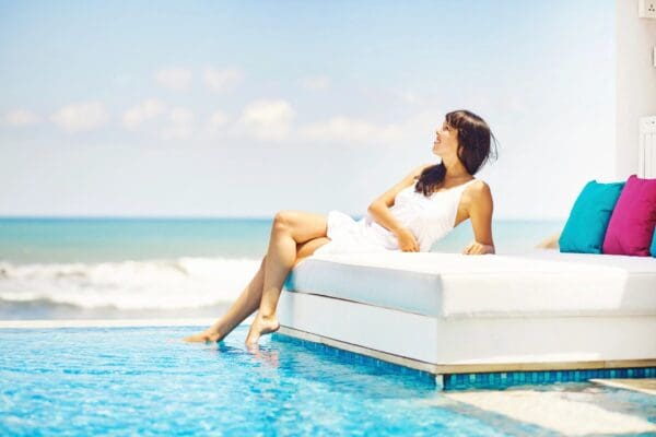 A woman sitting on top of a white couch near the ocean.