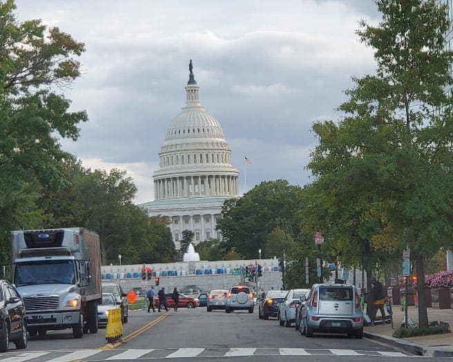 A street with cars parked on the side of it and a capitol building in the background.